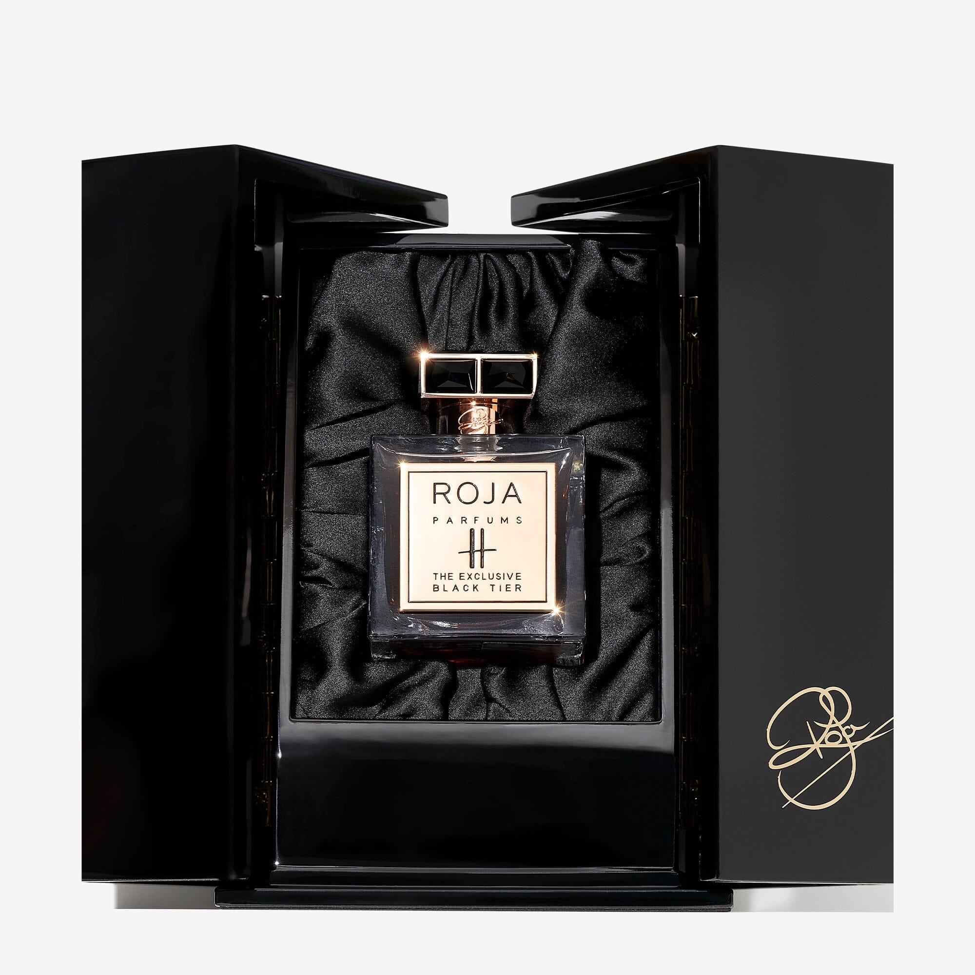 A bottle of Roja Parfums Harrods Black Tier perfume is showcased in an open black box lined with black satin and adorned with a gold signature on the lower right corner.