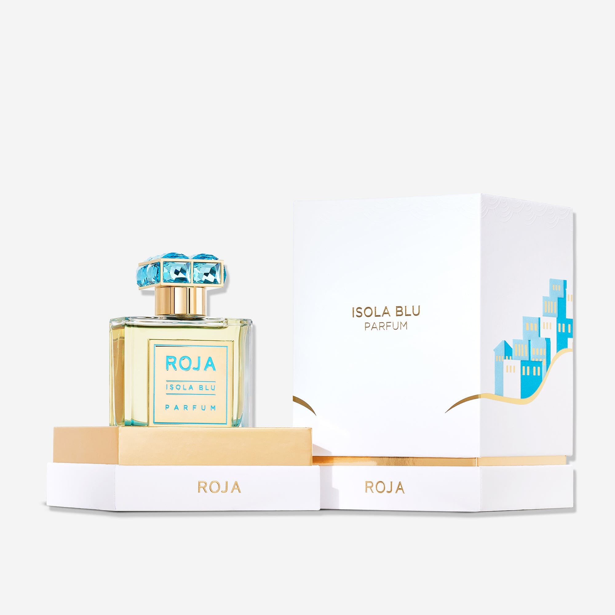 A bottle of Isola Blu by Roja Parfums, a citrus fragrance ideal for summer, rests on a white and gold box. Its matching packaging showcases blue houses and gold accents, evoking the feel of a five-star getaway.