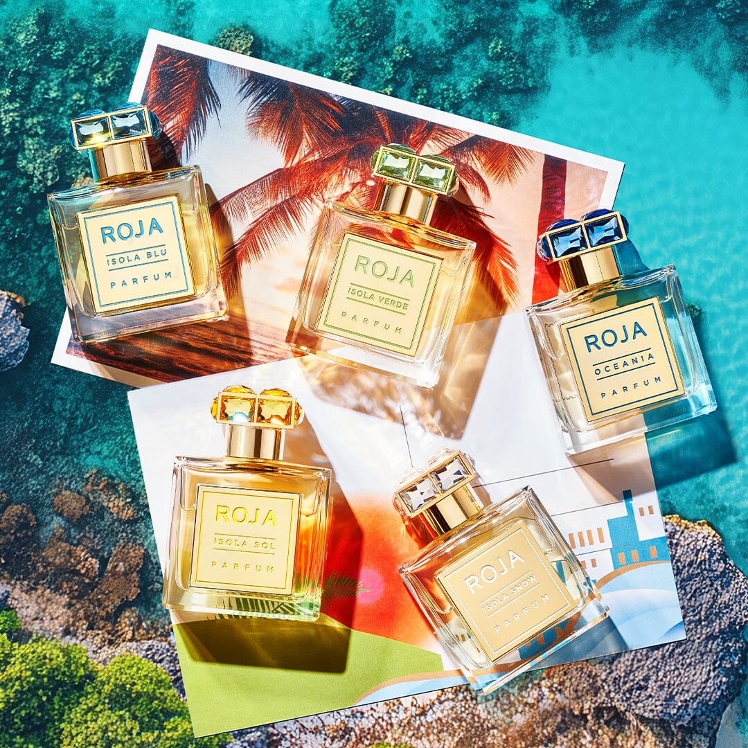 Five bottles of Isola Blu by Roja Parfums are displayed on colorful tropical and coastal postcards, set against a vibrant blue backdrop that evokes water and rocks—capturing the essence of a five-star getaway.
