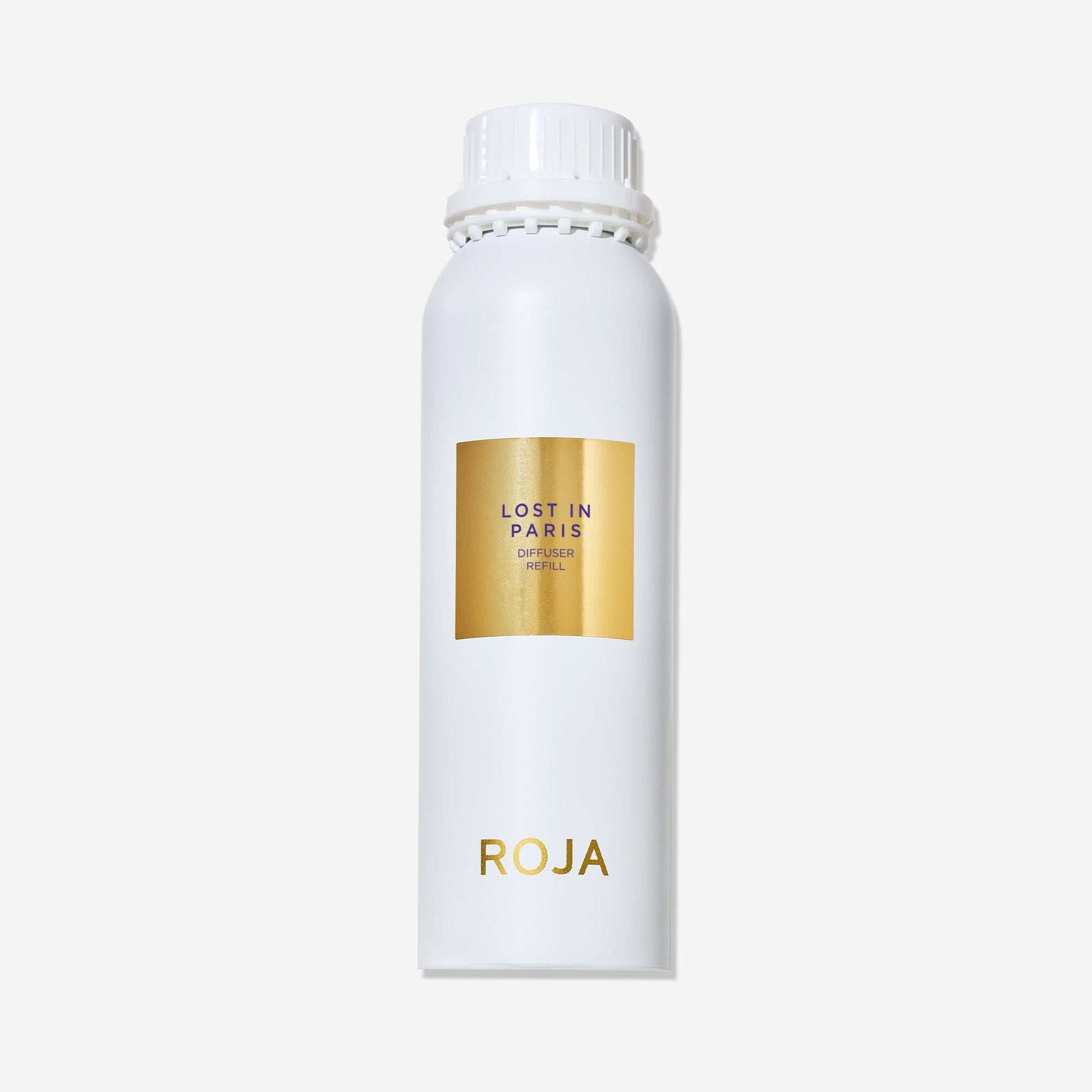 A white cylindrical bottle with a white cap displays a gold label reading Lost in Paris and ROJA London near the bottom. This ROJA London Lost in Paris diffuser captures a gourmand essence. The background is plain white.