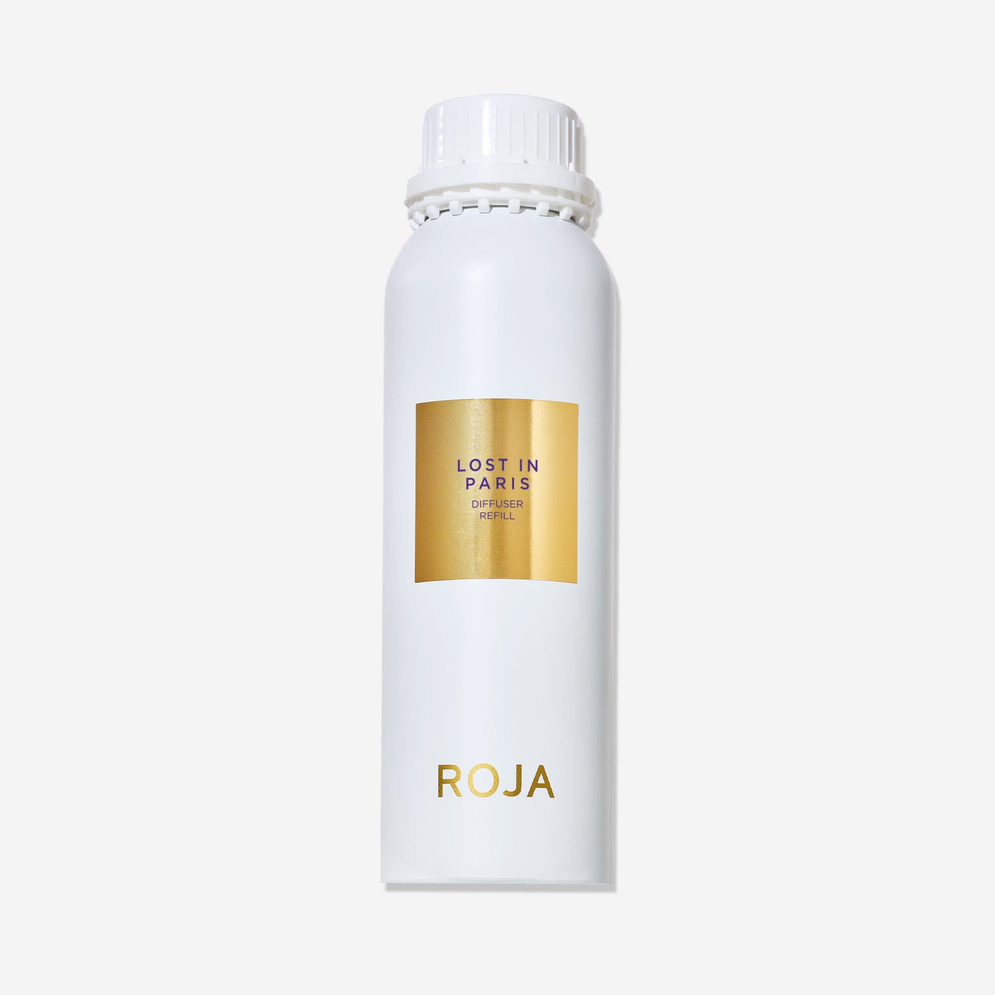 A white cylindrical bottle with a white cap displays a gold label reading Lost in Paris and ROJA London near the bottom. This ROJA London Lost in Paris diffuser captures a gourmand essence. The background is plain white.