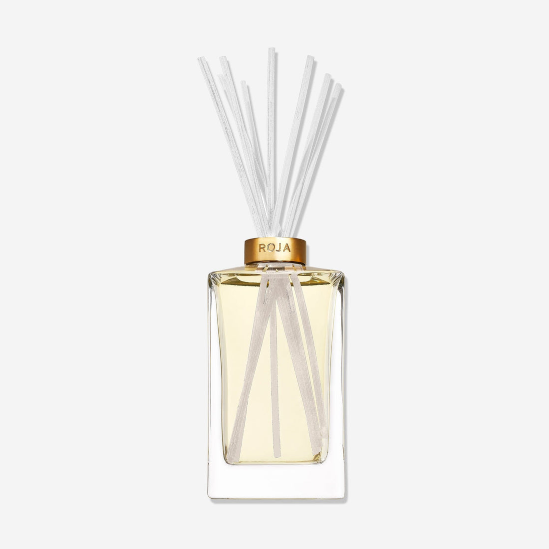 A clear ROJA London Lost in Paris diffuser with light yellow liquid, a gold ROJA collar, and thin white reeds. This gourmand fragrance exudes elegance against a plain white backdrop.