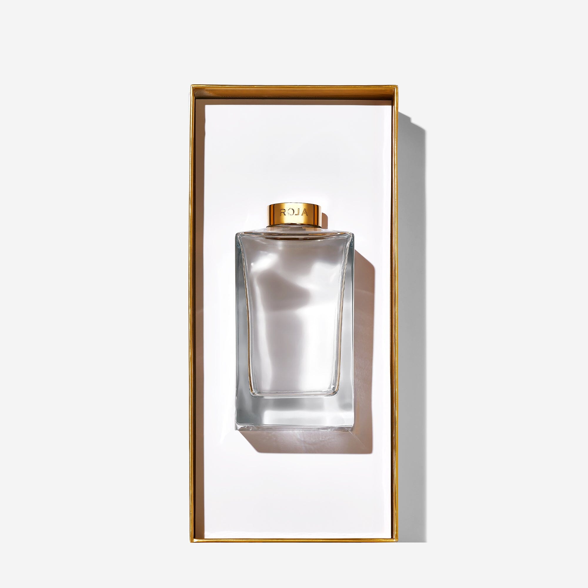 A clear rectangular perfume bottle with a gold cap, labeled ROJA London—Lost in Paris, rests in a white and gold box against a light background, creating an elegant display that suggests the luxurious gourmand scent inside.