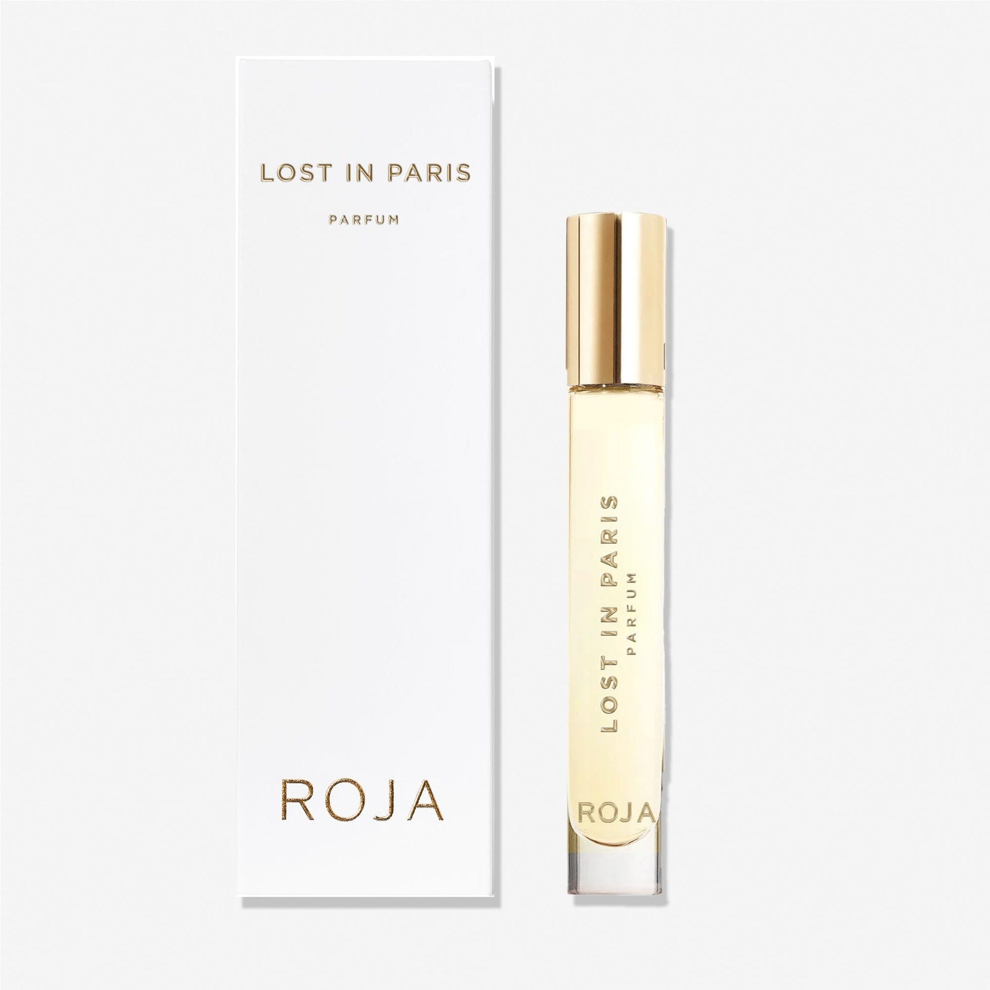 A clear perfume bottle with a gold cap labeled Lost in Paris stands beside its white box, both displaying gold text and the Roja Parfums brand—a tribute to Paris made from luxurious ingredients.