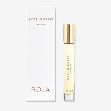 A clear perfume bottle with a gold cap labeled Lost in Paris stands beside its white box, both displaying gold text and the Roja Parfums brand—a tribute to Paris made from luxurious ingredients.