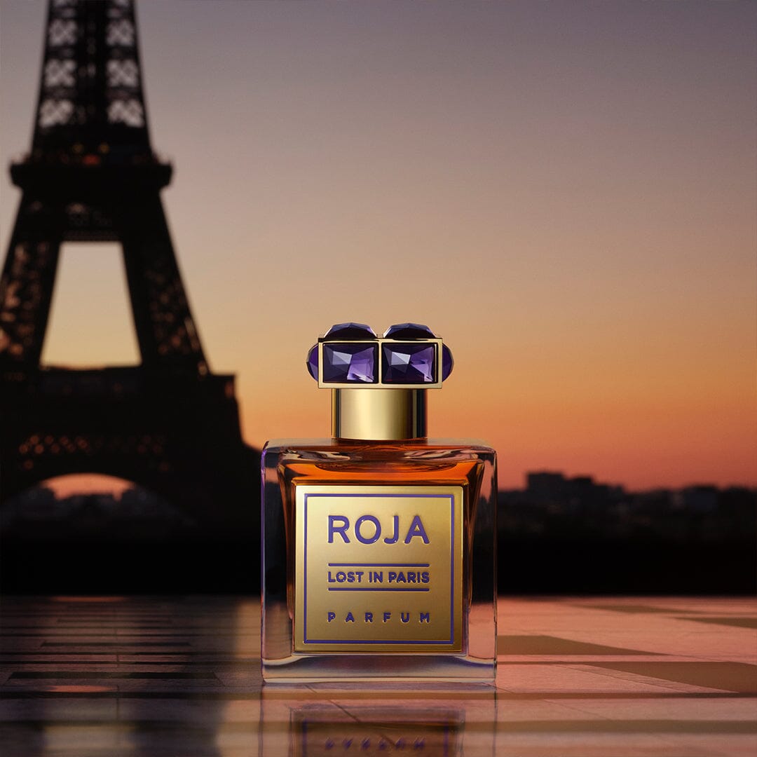 A bottle of Lost in Paris by Roja Parfums rests on a reflective surface, radiating gourmand notes, with the Eiffel Tower and a colorful sunset evoking Parisian high society in the background.