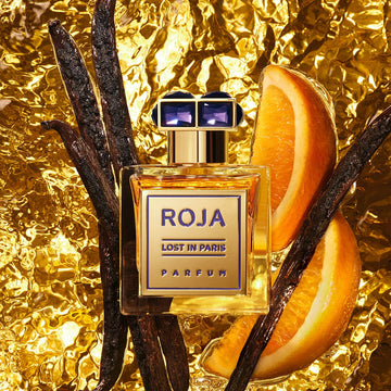 A bottle of Lost in Paris by Roja Parfums rests on gold foil, encircled by vanilla pods and orange slices, with a radiant golden background that suggests Parisian elegance and the richness of luxurious ingredients.