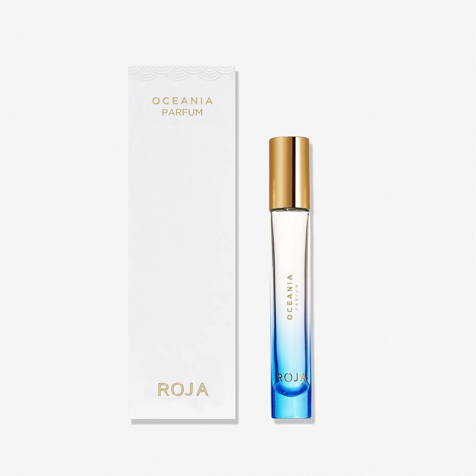 A blue gradient perfume bottle with a gold cap stands beside a white box labeled Oceania by Roja Parfums from the Isola Collection, inspired by olfactive islands, set against a plain white background.