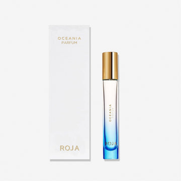 A blue gradient perfume bottle with a gold cap stands beside a white box labeled Oceania by Roja Parfums from the Isola Collection, inspired by olfactive islands, set against a plain white background.