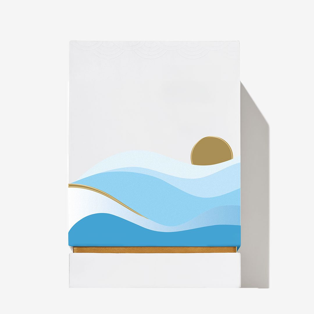 A minimalistic illustration on a white box shows stylized blue waves and a golden sun or moon rising above the horizon, with a simple, clean design inspired by Oceania from Roja Parfums.