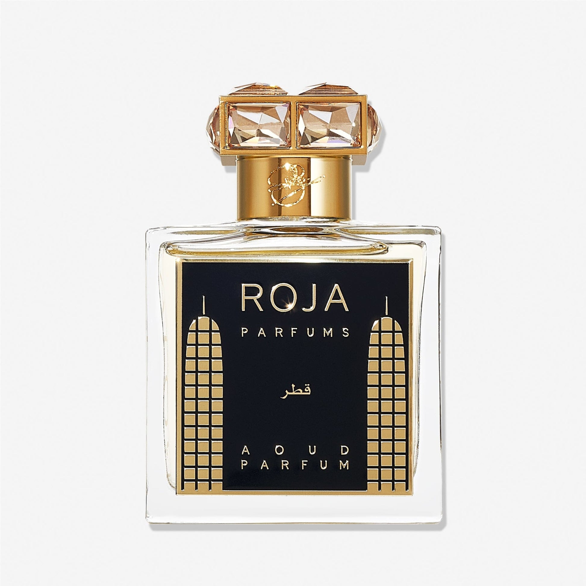 A luxury Roja Parfums Qatar perfume bottle features gold accents, geometric designs, and a crystal-studded gold cap—evoking notes of peach and pear in its lavish presentation.