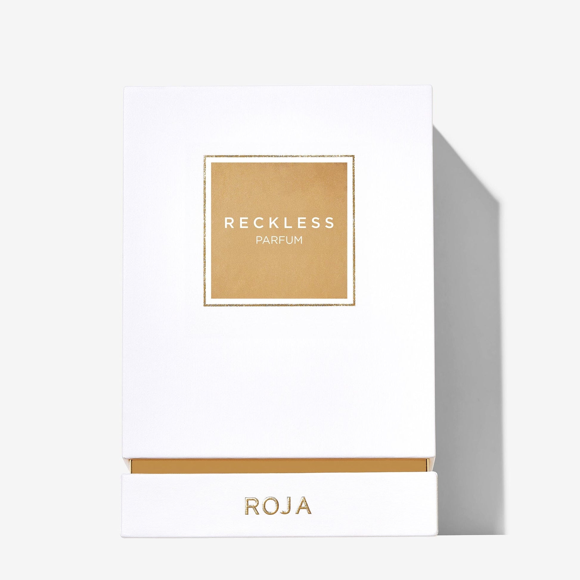 A white box with a gold square label reading Reckless Pour Femme and ROJA PARFUMS in gold on the bottom drawer, set against a light background—a summery fragrance with notes of vanilla and benzoin.