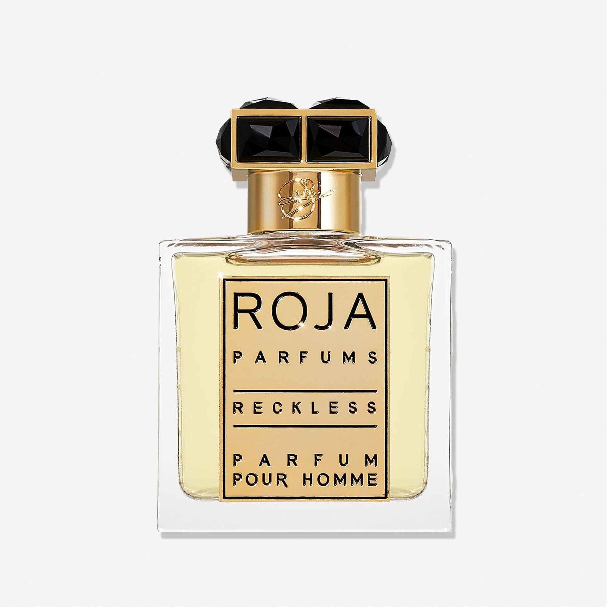 A clear glass bottle of Roja Parfums Reckless Pour Homme features a gold and black cap and holds light yellow liquid. The label shows the brand and product name in bold black letters—a masculine scent with spicy chypré notes.