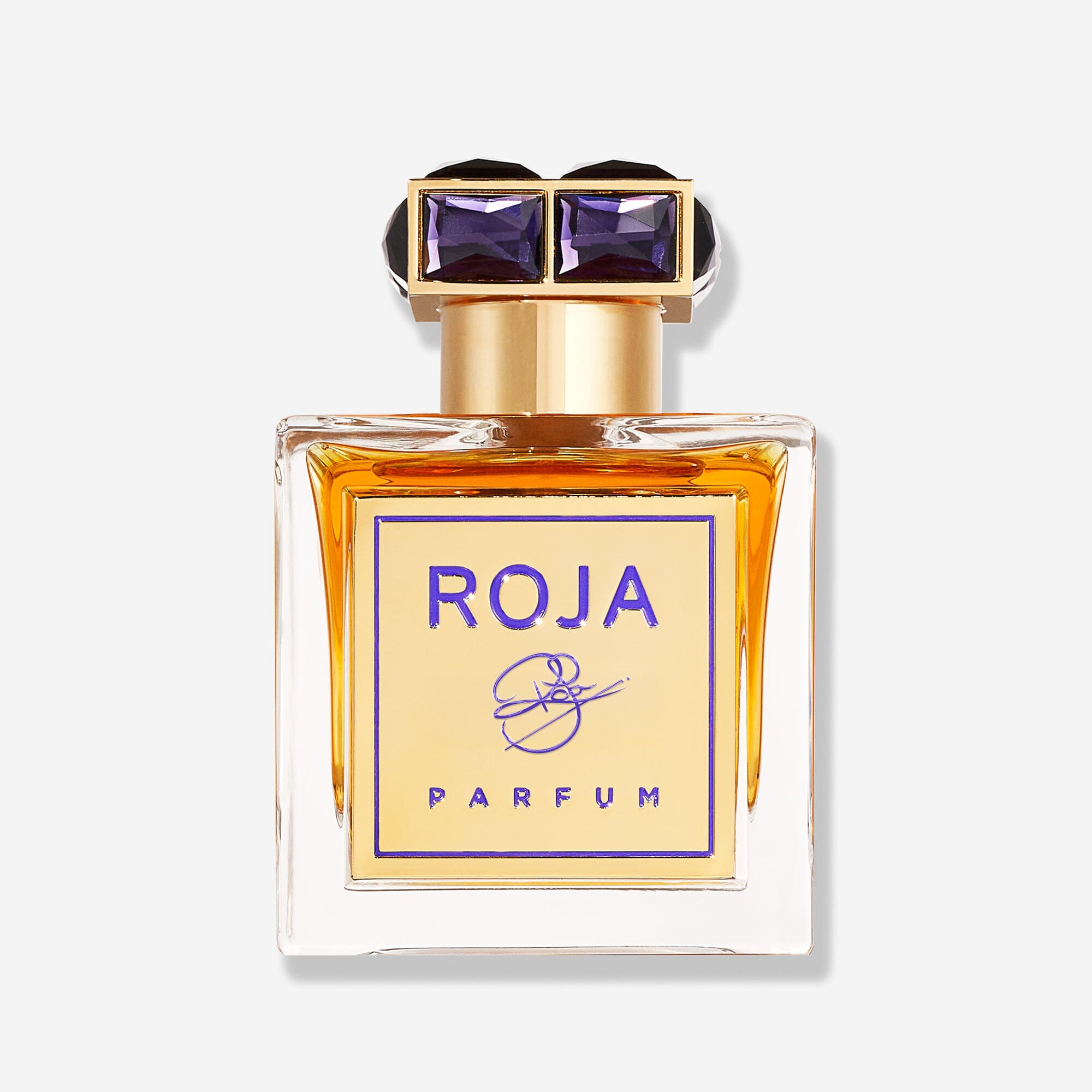 A glass bottle of ROJA by Roja Parfums, featuring amber liquid, a gold label with purple text, and a decorative black and gold geometric cap, set against a plain light background.