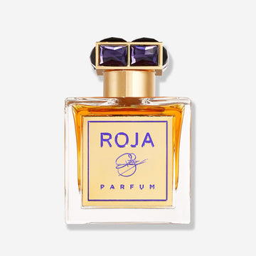A glass bottle of ROJA by Roja Parfums, featuring amber liquid, a gold label with purple text, and a decorative black and gold geometric cap, set against a plain light background.