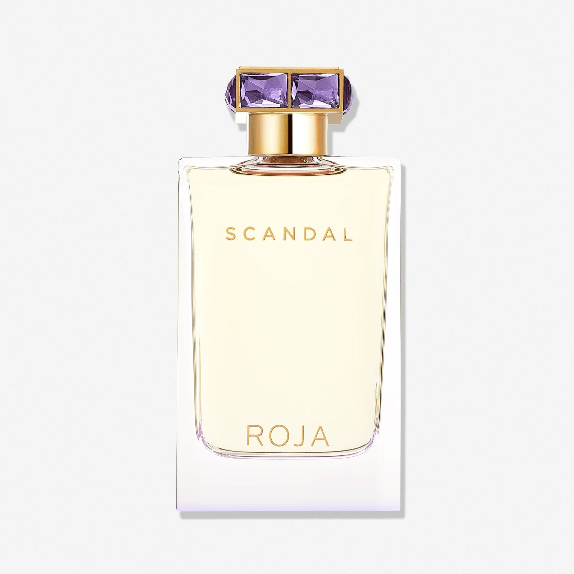 A rectangular bottle of Scandal Pour Femme by Roja Parfums, featuring gold lettering and a gold cap with purple gem-like details, exudes luxury and allure against a plain white background.