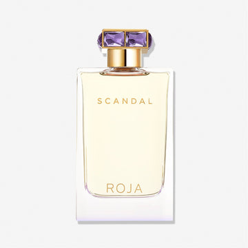 A rectangular bottle of Scandal Pour Femme by Roja Parfums, featuring gold lettering and a gold cap with purple gem-like details, exudes luxury and allure against a plain white background.