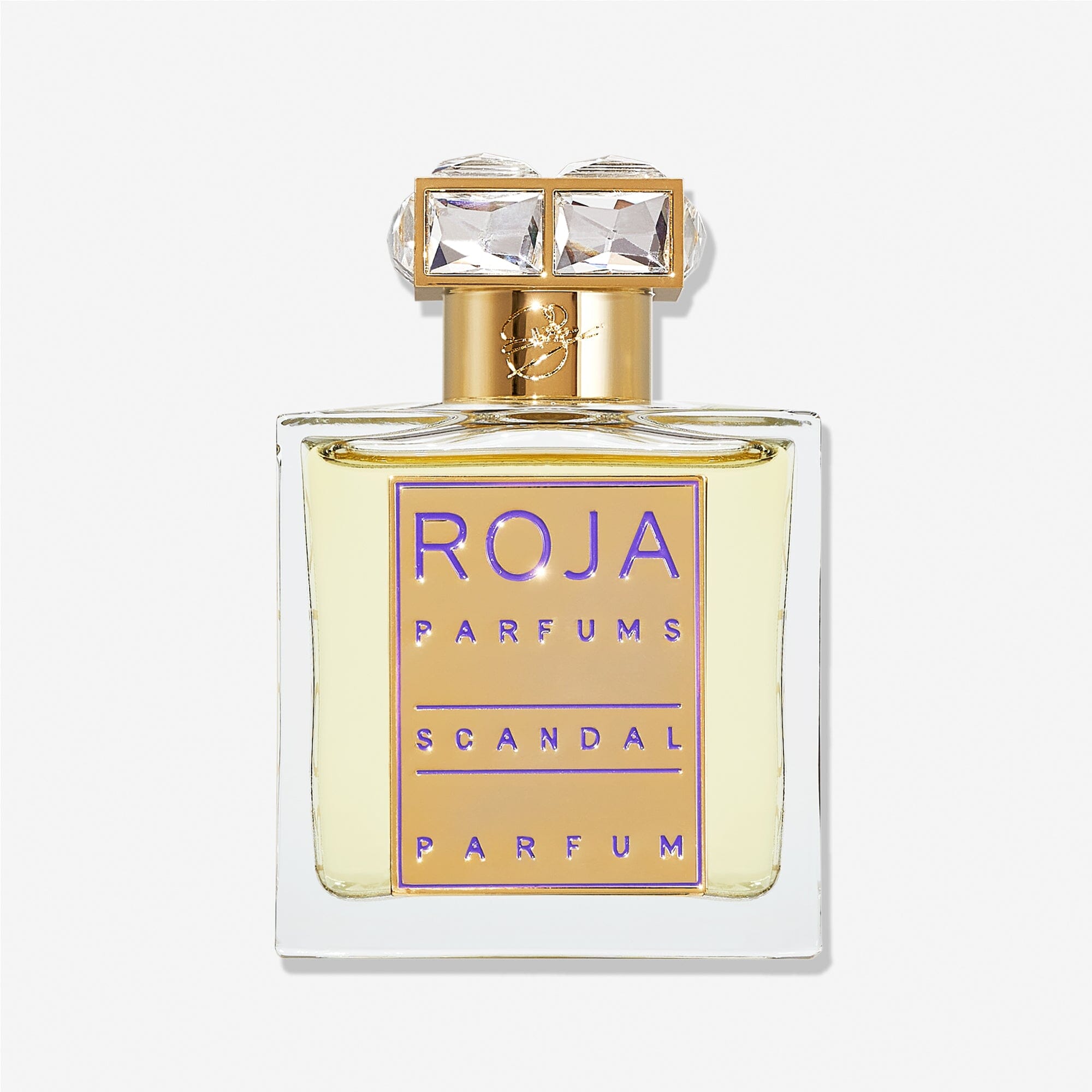 A clear glass bottle of Roja Parfums Scandal Pour Femme features a gold label with purple text and a gold cap set with two large, square, clear gemstones—an elegant nod to jasmine’s timeless allure.