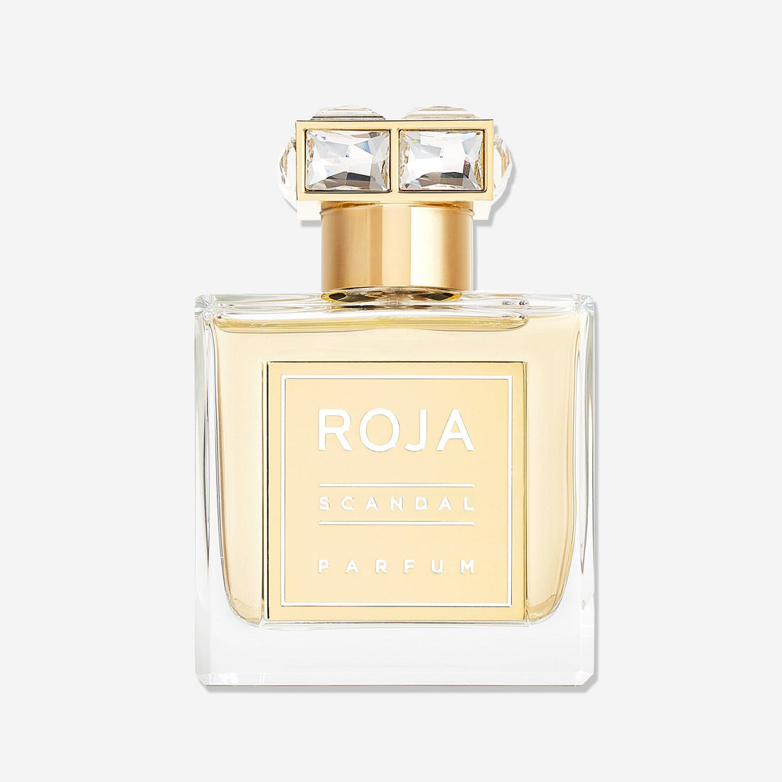 A clear glass perfume bottle with gold accents and a square gold label reading Roja Parfums Scandal Pour Femme. The gold cap features two large, clear rectangular gems, evoking the allure of narcotic white florals like jasmine and tuberose.