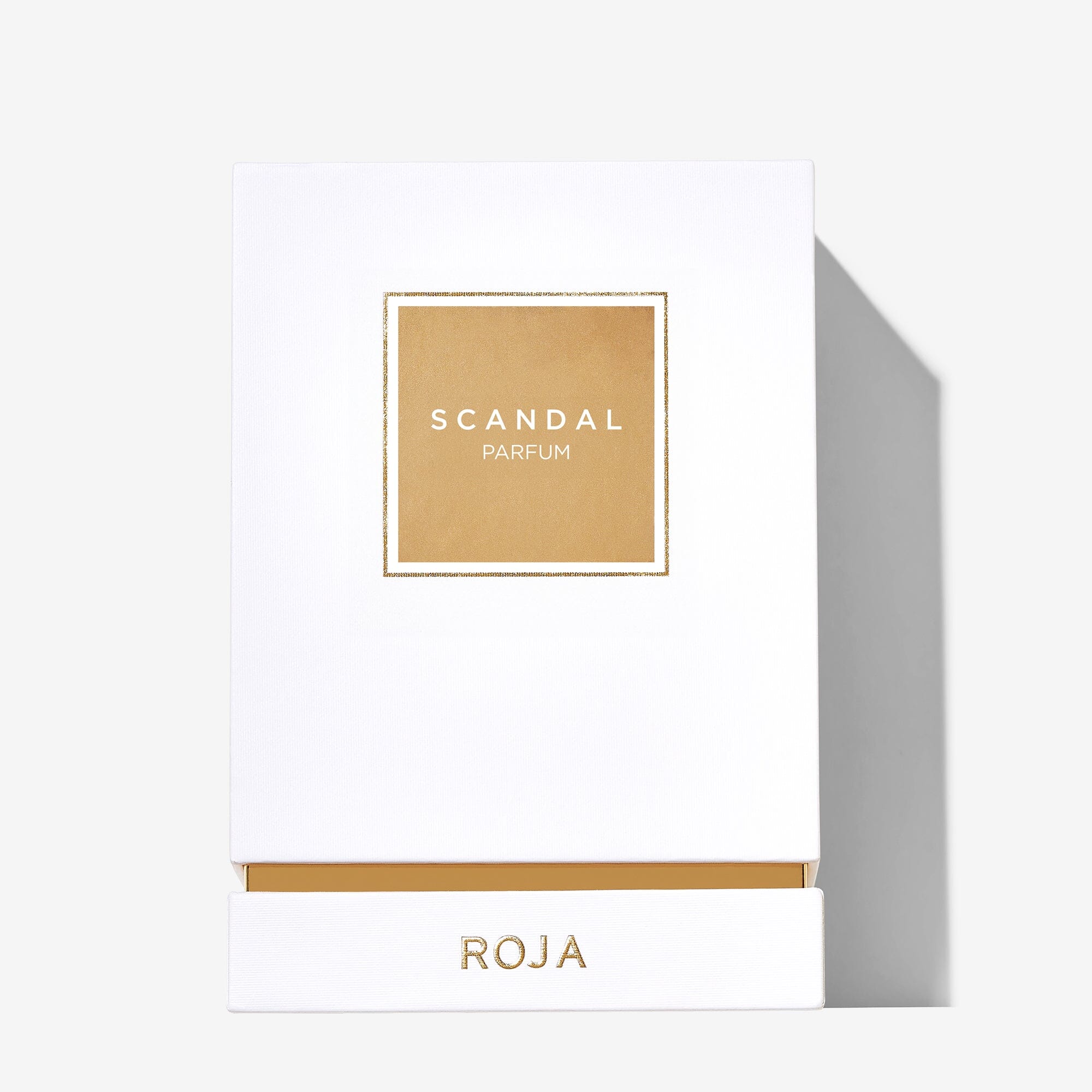 A white rectangular box with a gold SCANDAL PARFUM label and ROJA PARFUMS at the base reflects the minimalist elegance of Scandal Pour Femme by Roja Parfums, hinting at its refined white flower fragrance inside.