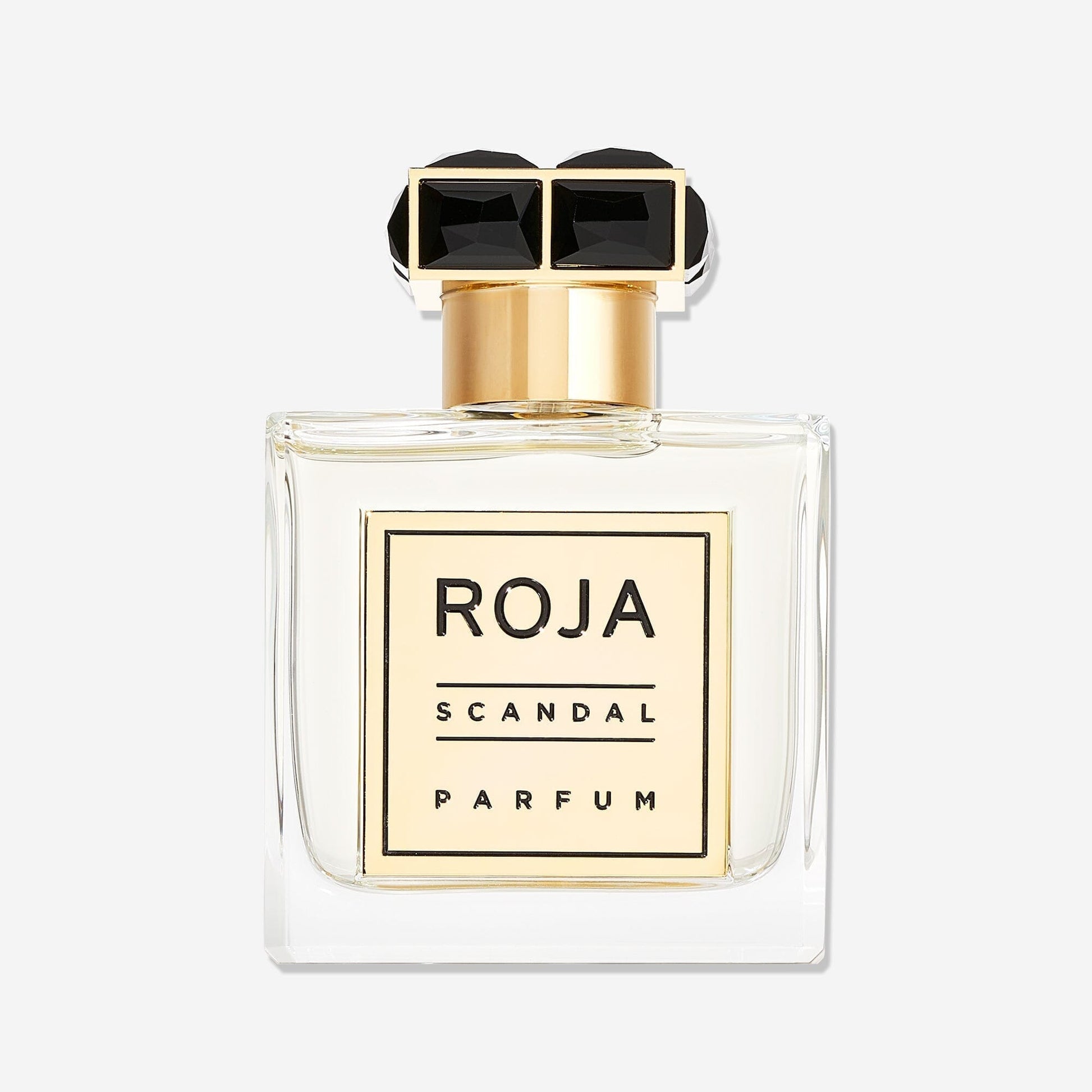 A clear glass bottle of Roja Parfums Scandal Pour Homme with a gold and black geometric cap. The label reads "Roja Parfums Scandal Pour Homme"—a sophisticated fougère fragrance for the modern gentleman.