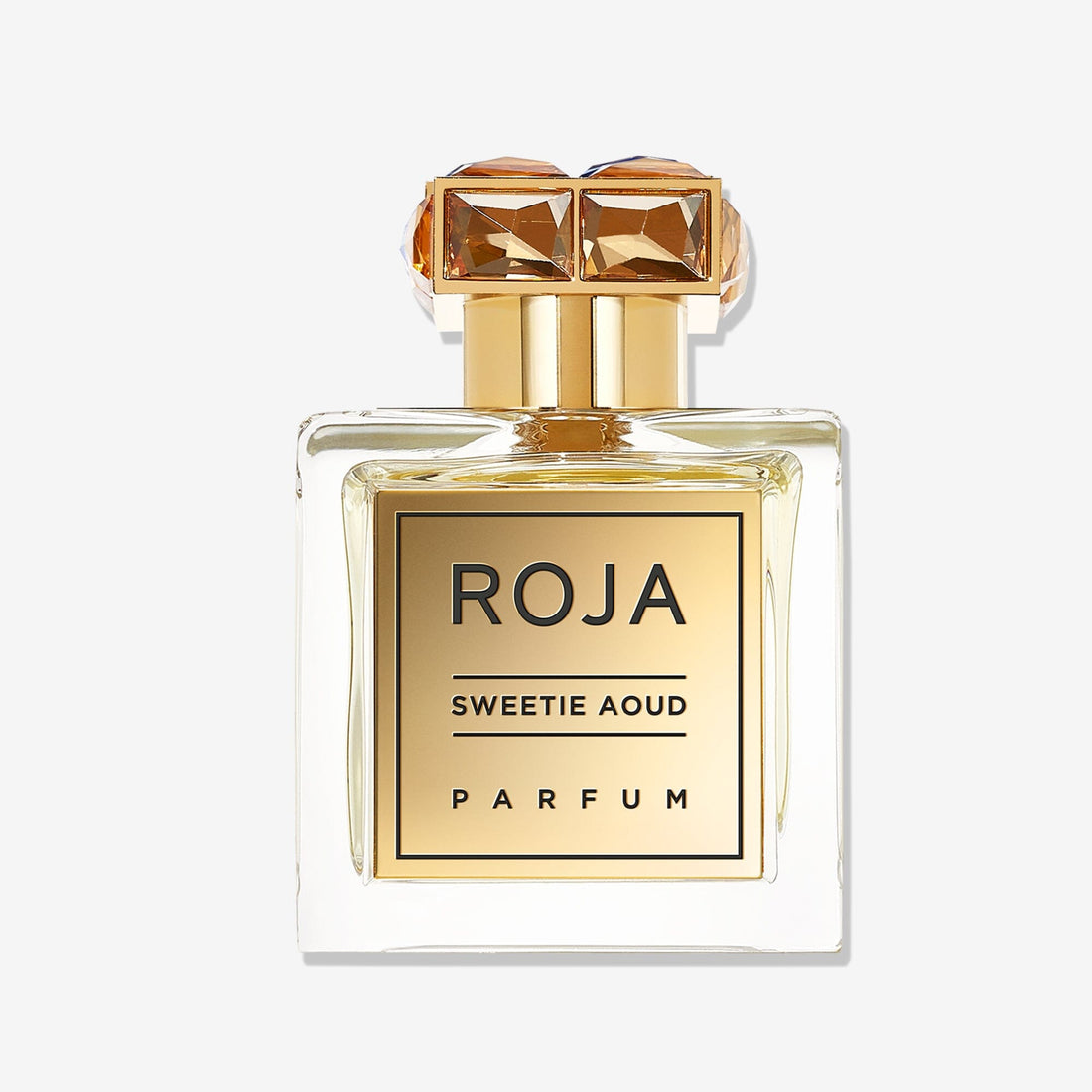 A clear glass bottle of Roja Parfums Sweetie Aoud, with a gold label and cap adorned by two square amber gemstones, stands against a plain white background.