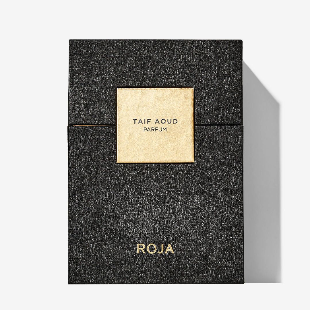 A black textured perfume box with a gold label reading Taif Aoud Parfum evokes Arabian rose and frankincense. Roja Parfums is in gold at the bottom, and the box casts a shadow on a white background.