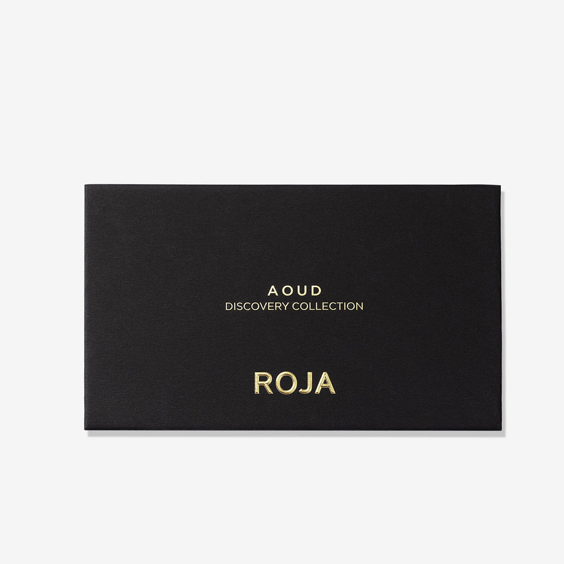 A sleek black rectangular box with gold text displays “The Aoud Discovery Collection” and “Roja Parfums” on the front, captured against a crisp white background—a refined prelude to the renowned Aoud Discovery Collection, inviting you to discover an expertly selected array of oud fragrances reminiscent of Arabian opulence.