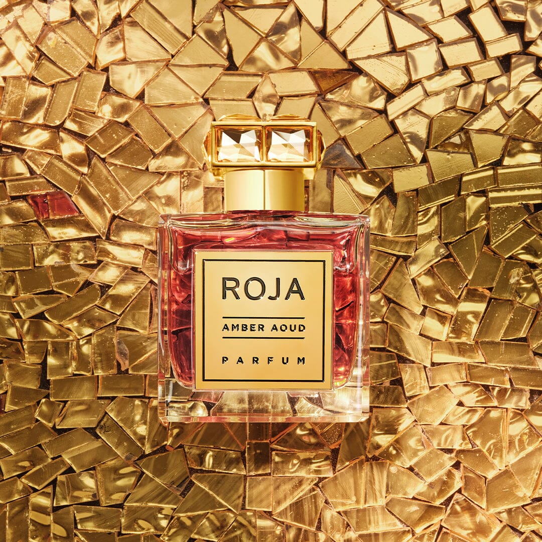 The Aoud Layering Gift Set by Roja Parfums, featuring a gold-capped bottle with a gold label, is displayed against a shimmering textured gold mosaic background, capturing the luxurious essence of oud and rare Agar Wood.