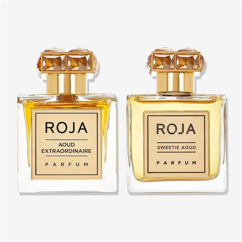 Two glass perfume bottles with gold labels—The Art of Layering Aoud by ROJA London—stand side by side, each topped with a faceted golden cap. Experience the luxurious scent of Agar Wood with this signature ROJA duo.