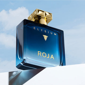 The Elysium Gift Set by Roja Parfums, featuring a blue glass bottle with a gold cap, is displayed against a bright sky on a white surface—ideal for fragrance layering.