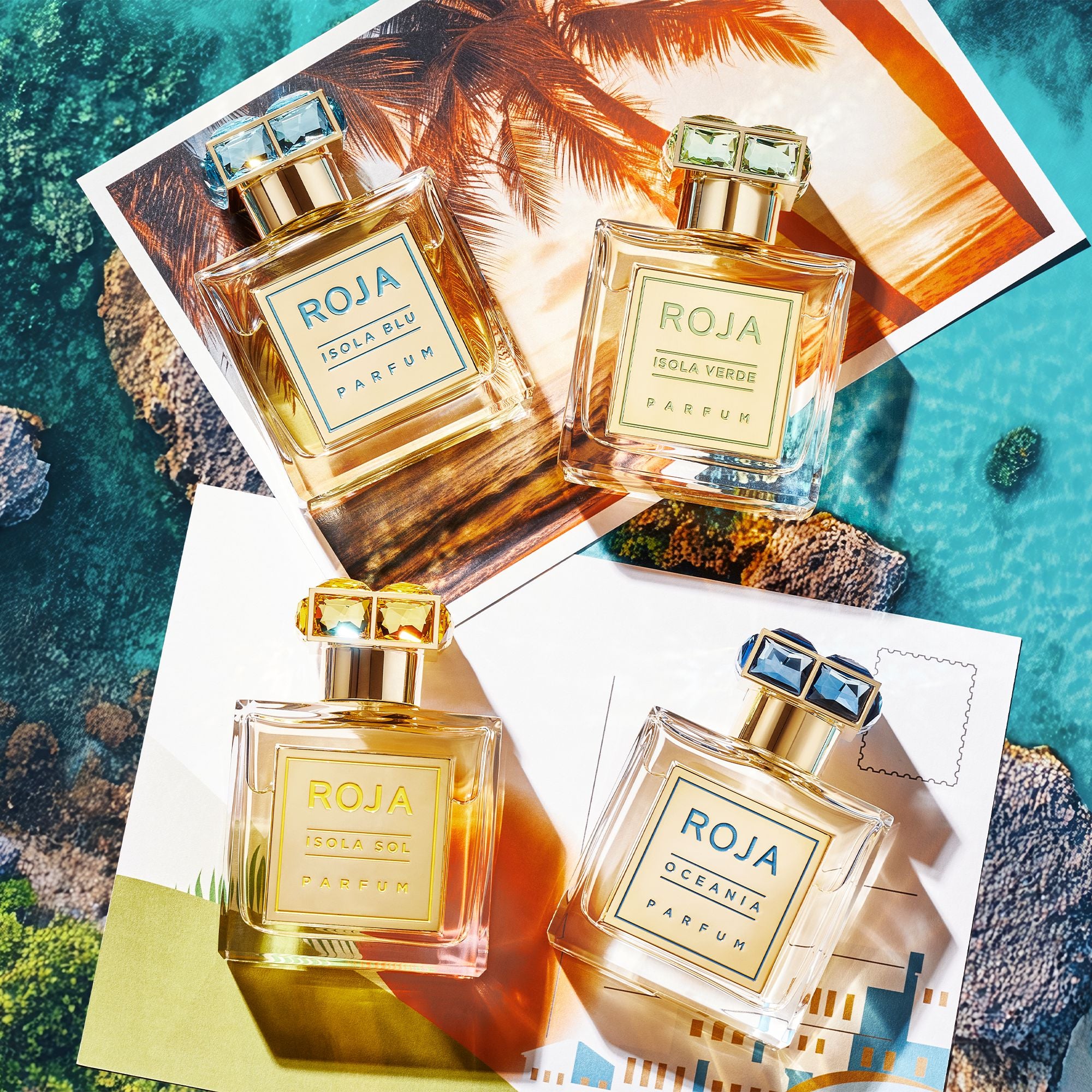 Four bottles from Roja Parfums Isola Travel Collection rest on tropical postcards, inviting you on a sensory journey with blue ocean waves, palm trees, and a rocky coastline in the background.