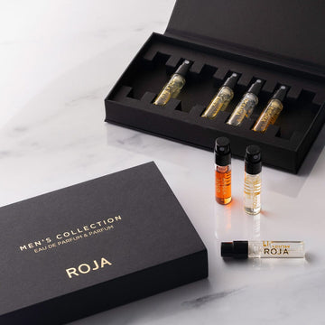 A black box labeled The Mens Discovery Collection by Roja Parfums holds five perfume vials, with three displayed outside on a white marble surface.