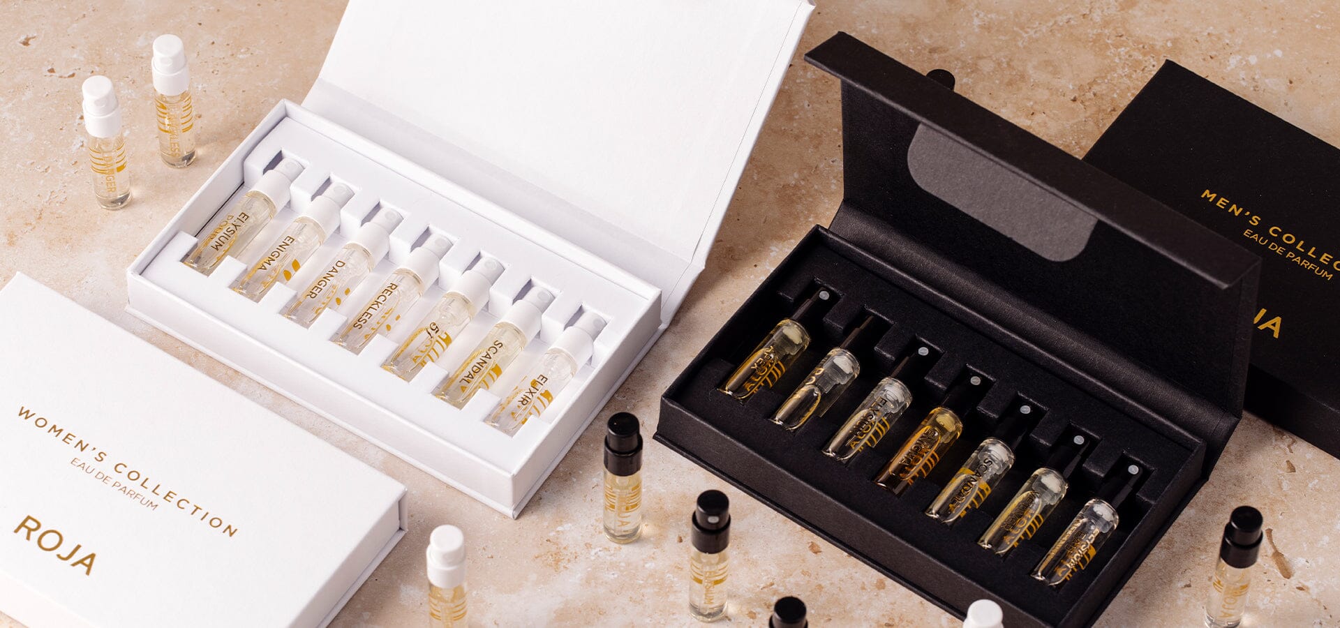 Two open cases display small perfume sample vials: a white box labeled Womens Collection and a black box labeled Mens Collection. Extra vials are scattered on a marble surface.