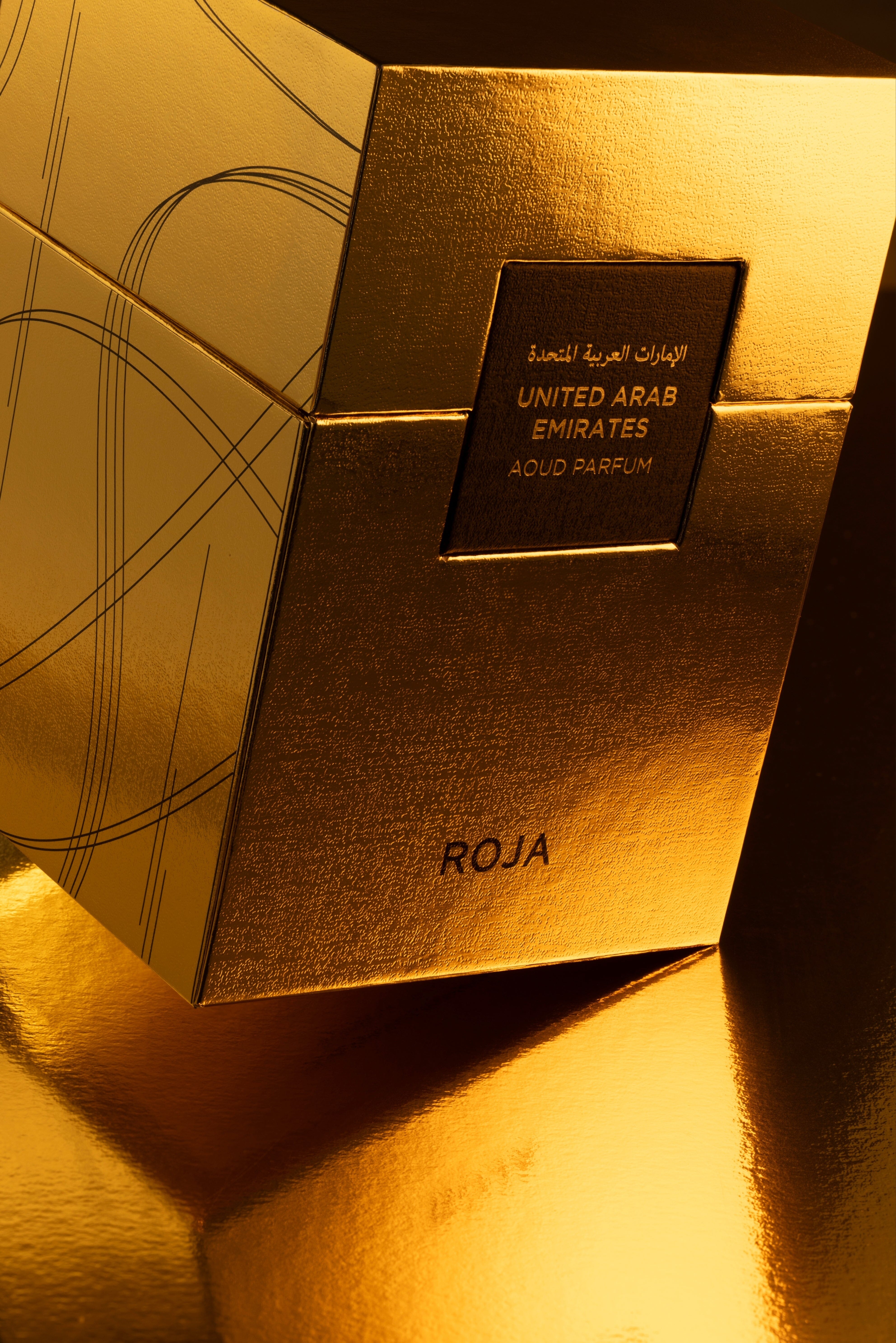 A luxurious gold perfume box from Roja Parfums, elegantly labeled "United Arab Emirates" in black text, rests on a reflective gold surface—capturing the opulent essence of oud mingled with warm frankincense.
